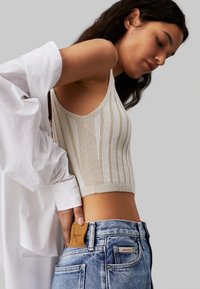 Top corto de color beige claro con relieve vertical, combinado con jeans de mezclilla azul de tiro alto que presentan una etiqueta de cuero.