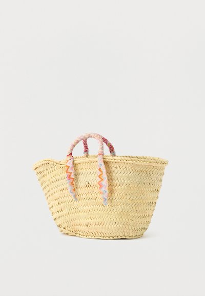 Πλεκτή τσάντα ώμου από ψάθα με φαρδιά βάση και κοντά χερούλια καλυμμένα με πολύχρωμο ύφασμα με ζιγκ-ζαγκ, φόντο σε απλό χρώμα.