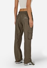 Olivinės spalvos cargo kelnės su laisvu kirpimu, kuriuose yra kelios kišenės, detali siuvinėjimas ant užpakalinių kišenių ir reguliuojami apatiniai raiščiai.