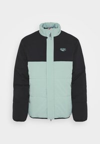 Veste rembourrée avec une partie supérieure noire et une partie inférieure vert menthe. Elle possède un col haut, une fermeture éclair intégrale et un détail logo sur la poitrine.