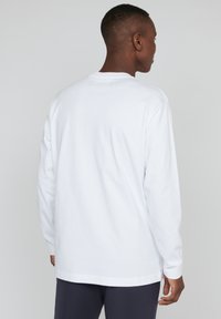 Balta medvilninė marškinė su ilgomis rankovėmis, apvaliu kaklu, laisvu siluetu ir tiesiu apvadu. tekstūruotas audinys su minimaliais siuvinėjimo detaliais.