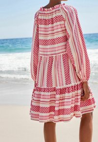 Vestido fluido con mangas largas abullonadas, que presenta atrevidos patrones geométricos en rojo y blanco, escote elástico y dobladillo con volantes.