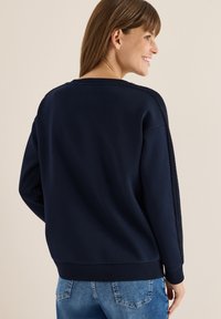 Mørkeblå sweatshirt med tekstureret sidelining, ribbede manchetter og kant. Glat stof, afslappet pasform, synlig sømstruktur på bagsiden.