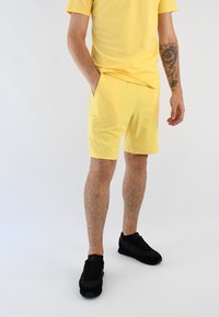 Camiseta de algodón amarilla y pantalones cortos a juego, ambos en corte relajado. Zapatillas deportivas negras. Diseño sencillo sin patrones ni acentos visibles.