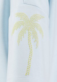 Manga de tela azul claro con un diseño de palmera formado por pequeños puntos amarillos en relieve, organizados por tamaño y forma.