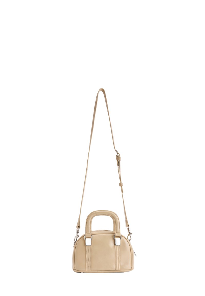 Beige kleine handtas met gebogen bovenkant, dubbele korte handvatten, zilverkleurige hardware en een verstelbare lange schouderriem op een witte achtergrond.
