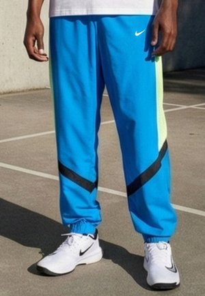 Person som har på seg lyseblå treningsbukser med svarte chevronstriper og hvite Nike-sneakers, stående på en utendørs bane.