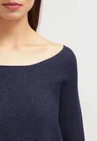 Top in maglina a coste blu navy con design scellato, caratterizzato da una superficie testurizzata e un ampio scollo. Il tessuto sembra morbido e aderente.