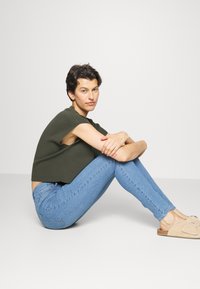 Olíva zöldCrop top, világoskék skinny farmernadrág, bézs slip-on cipő szív díszítéssel. Rövid ujjú és laza fazonú.