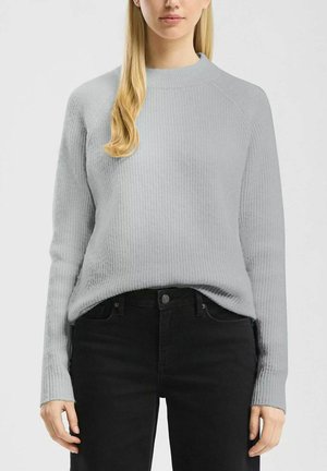 Maglione grigio chiaro a coste con collo alto e maniche lunghe, abbinato a jeans neri. Il maglione presenta un tessuto testurizzato e una vestibilità comoda.