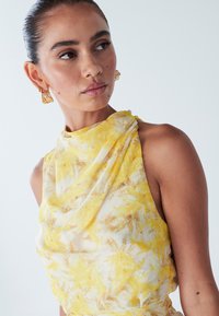 Geel bloemenblouse van lichtgewicht stof, met een asymmetrische halslijn en een gladde textuur, aangevuld met gouden oorbellen.