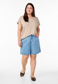 Beiger T-Shirt mit kurzen Ärmeln, kombiniert mit hellblauen Jeansshorts. Der Look wird durch flache Schuhe mit Animal-Print abgerundet.