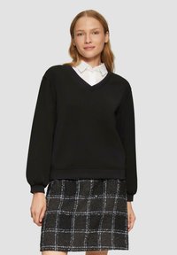 Czarny sweter z dekoltem w serek oraz długimi, bufiaste rękawami, zestawiony z czarną spódnicą w kratkę z białymi i niebieskimi akcentami.