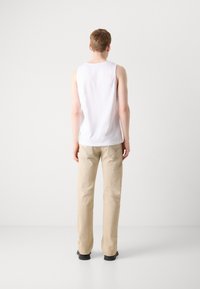 Witte mouwloze tanktop en beige broek, met een rechte snit, met zichtbare stikdetails en zwarte schoenen. Achteraanzicht.