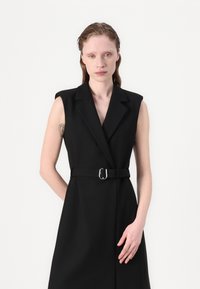 Black sleeveless dress with a fitted waist and silver buckle belt, featuring a sharp lapel collar and clean, structured design.