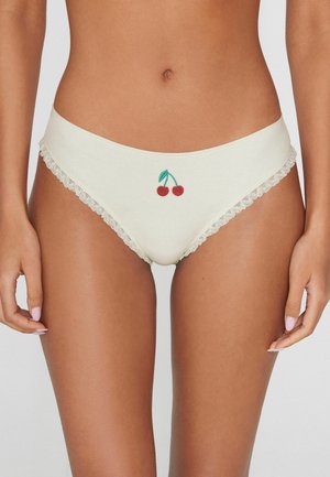 Frau trägt cremefarbene Unterwäsche mit Spitzenbesatz und einem kleinen, bestickten Kirschmotiv vorne in der Mitte.