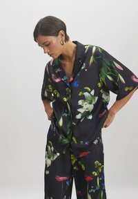Schwarz mit floralem Muster, Set bestehend aus Hemd und Hose aus Satin. Merkmale sind lebhafte Blumen in Pink, Weiß, Blau und Grün. Mit Knopfleiste, lockerer Schnitt.