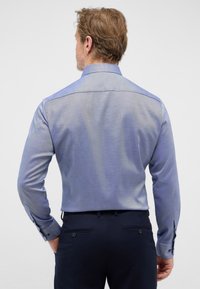 Heren overhemd met lange mouwen in lichtblauw, van een gestructureerde stof met een subtiel ruitpatroon, voorzien van een button-down kraag en contrasterende manchetten.