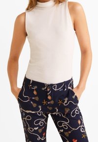Haut sans manches beige clair à côtes, associé à un pantalon bleu marine à motifs d'inspiration marine colorés et ornés de dessins de cordages entrelacés.