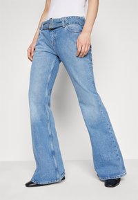 Jeans acampanados de color azul claro con cinturón, que presentan una cintura alta, cinco bolsillos y un ligero desgastado en el frente. Textura de mezclilla con detalles de costura.