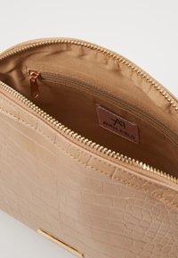 Borsa beige con motivo coccodrillo e cerniera dorata, con interno liscio e etichetta con il nome del marchio "ANNA FIELD".