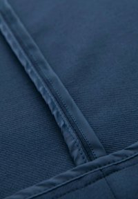 Närbild av en blå tygdragkedja med detaljerad sömnad och en texturerad materialbakgrund.