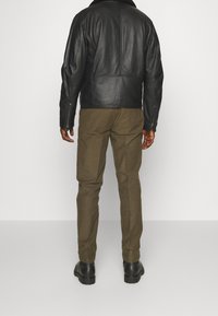 Svart läderjacka med ståkrage, kombinerad med olivgröna byxor och svarta stövlar. Jackan har dragkedjeärmar och en skräddarsydd passform.