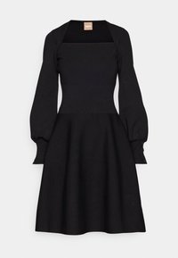 Robe en maille noire avec encolure carrée, manches longues bouffantes, taille ajustée et jupe évasée, présentée sur un fond gris clair.