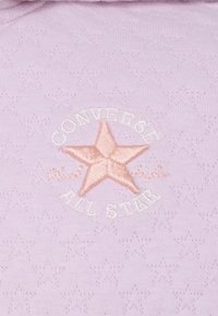 Tessuto di cotone lavanda con un logo a stella ricamato rosa e il testo "Converse All Star", su uno sfondo testurizzato.