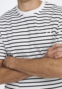 Hvid t-shirt med sorte vandrette striber, rund halsudskæring og et lille broderet logo på brystet. Blødt bomuldsstof.