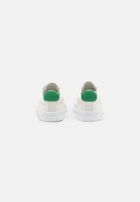 Zapatillas blancas con acentos verdes en el talón y paneles de tela texturizada. Presentan una suela de goma blanca y un logo en relieve en el talón.