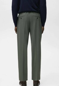 Pantalones verdes plisados con un ajuste entallado, que presentan dos bolsillos traseros con botones. La tela parece lisa con un acabado mate.