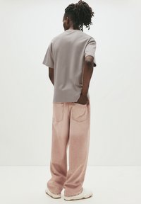 Grå kortærmet t-shirt parret med lys rosa vide bukser. Glat stoftekstur, afslappet pasform og to baglommer på bukserne.