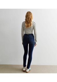 Jeans skinny de tiro alto en azul oscuro con un ajuste ceñido y bolsillos traseros tradicionales, combinados con una camiseta de rayas de manga larga.