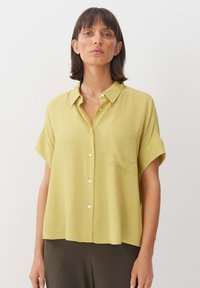 Camicia a maniche corte in tessuto giallo chiaro con chiusura a bottoni sul fronte, taschino singolo sul petto e vestibilità ampia e rilassata.