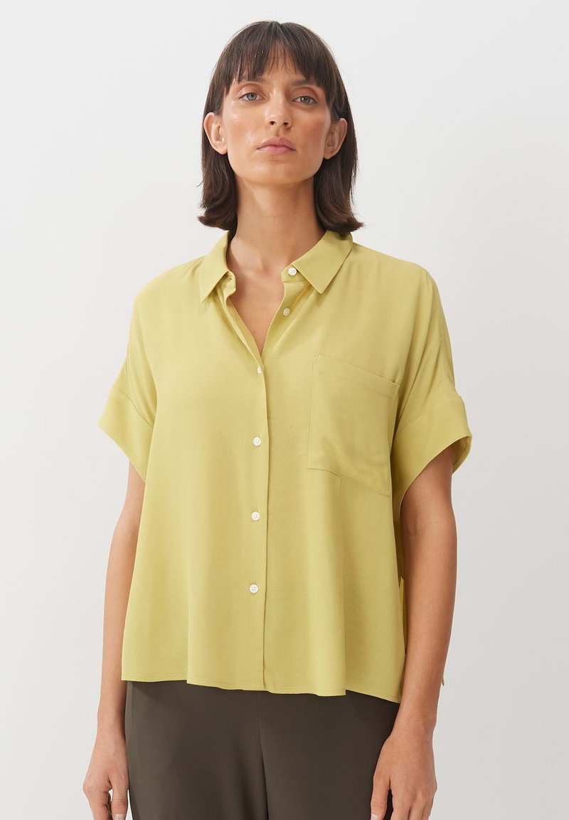 Camicia a maniche corte in tessuto giallo chiaro con chiusura a bottoni sul fronte, taschino singolo sul petto e vestibilità ampia e rilassata.