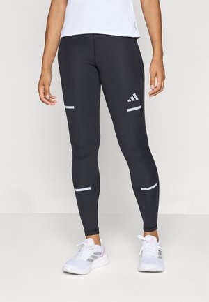 Zwarte sport leggings met reflecterende zilveren accenten, met een nauwsluitende pasvorm en een gladde textuur. Gecombineerd met witte sneakers.