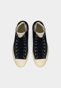 Μαύρα ψηλά αθλητικά παπούτσια με λευκά κορδόνια, εκρού κάλυμμα στη μύτη και αντίθετη λευκή ραφή. Πανί πάνω μέρος με επίπεδη λαστιχένια σόλα.