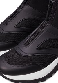 Černé sportovní boty se zipem, síťovanými panely a texturovanou gumovou podrážkou s výrazným bílým pruhem.