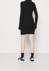 Robe noire côtelée à manches longues, col montant, coupe ajustée et ourlet festonné. Associée à des baskets rayées noir et blanc et des chaussettes assorties.