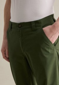 Groene katoenen broek met een zijzak, knoopsluiting en subtiele textuur; ontworpen voor een relaxte pasvorm met een gladde afwerking.
