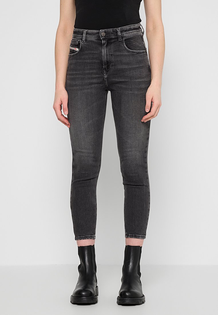 Schwarze Skinny-Jeans mit subtiler Ausbleichung, hoher Taille, Fünf-Taschen-Design, ausgefranster Saum, kombiniert mit schwarzen Knöchelschuhen. Glatte Denim-Textur.