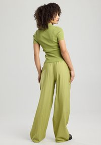 Green ribbed knit top with short sleeves paired with loose, lightweight green trousers. Both garments have a soft texture and relaxed fit.