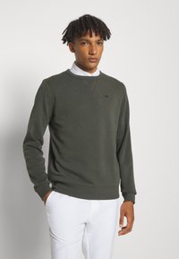 Mørkegrønn sweatshirt i et glatt stoff, design med rund hals, med ribbede mansjetter og kant, og med en liten svart logo på brystet.