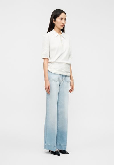 Polo blanc à côtes avec manches courtes, patte de boutonnage, associé à un jean large bleu clair et des escarpins noirs à bout pointu.