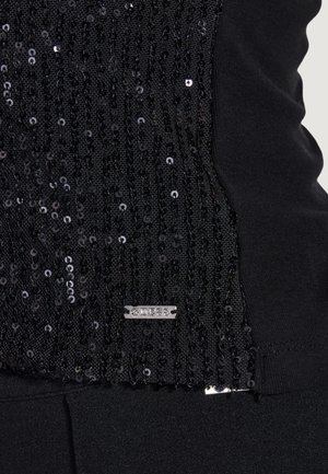 Czarna tkanina z pionowymi rzędami małych czarnych cekinów oraz małą prostokątną metalową metką blisko dolnej krawędzi.