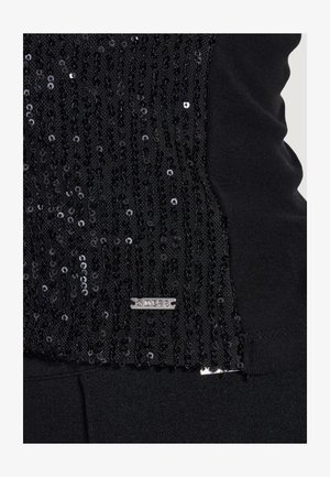 Czarna tkanina z pionowymi rzędami małych czarnych cekinów oraz małą prostokątną metalową metką blisko dolnej krawędzi.