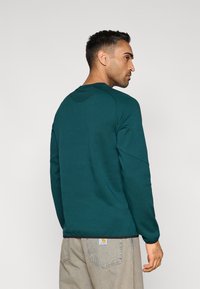 Πράσινο φούτερ με μακριά μανίκια, στρογγυλή λαιμόκοψη και ριμπ λεπτομέρεια στους ώμους, συνδυασμένο με ανοιχτόχρωμο, φαρδύ τζιν.