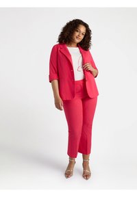 Blazer fucsia con maniche arrotolate e pantaloni abbinati con un sottile motivo a pois. Top bianco con un design a contorno rosso. Sandali metallici con cinturini.