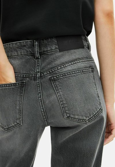 Jeans de mezclilla gris oscuro con un corte relajado, que presentan bolsillos traseros, costuras visibles y una etiqueta de marca de cuero negro en la cinturilla.